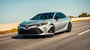 Modern silver Toyota Camry hybrid sedan driving on sunny highway with clear sky, showing sleek aerodynamic profile and front angle view