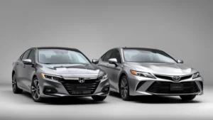 Professional studio photograph of 2024 Honda Accord and Toyota Camry sedans positioned side by side, showcasing midsize sedan proportions and contemporary styling details, neutral gray background, natural lighting highlighting body lines and design elements