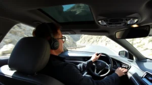 Professional automotive journalist testing a luxury sedan on a winding mountain road, focused driving position, natural daylight, premium interior visible through windshield