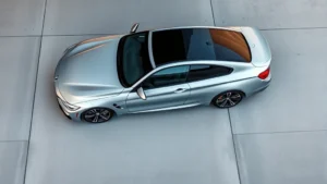 Overhead view of a sleek silver BMW M440i sports sedan parked on a modern concrete surface, showcasing its aggressive body lines and multi-spoke wheels in natural daylight